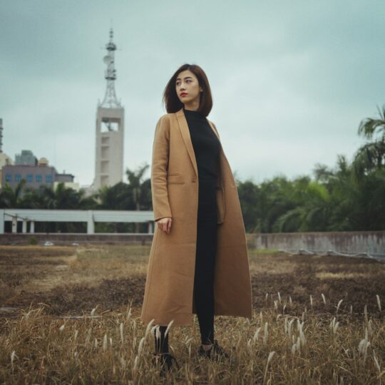 woman wearing brown coat standing on brown grass