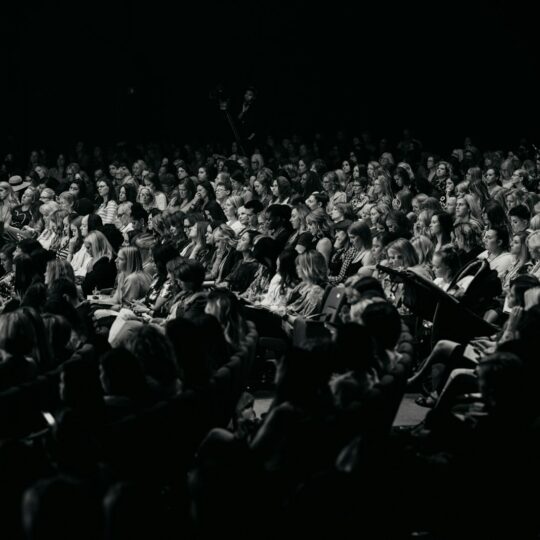 An audience watches a performance in a dark theater