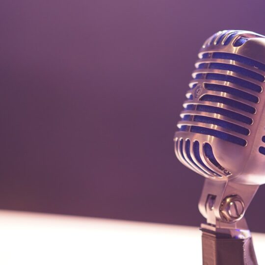 A vintage silver microphone with blue accents against a soft purple background