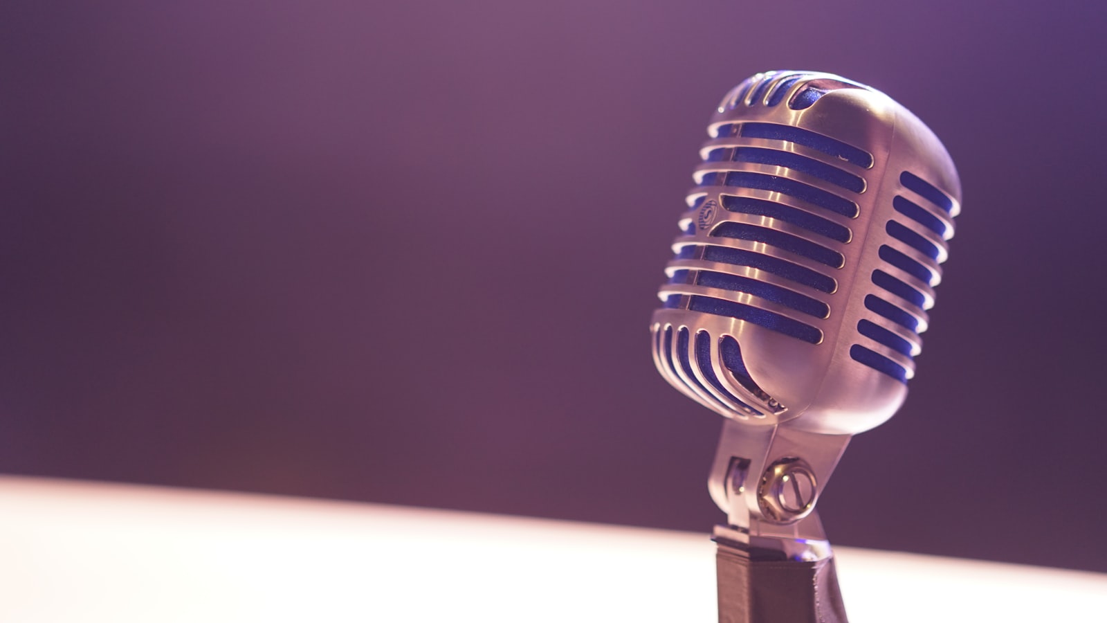 A vintage silver microphone with blue accents against a soft purple background