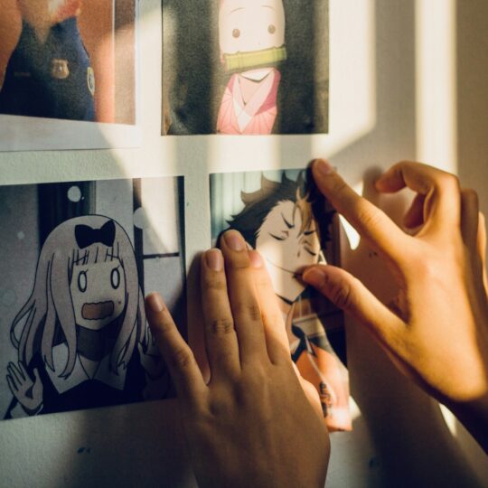 Hands attaching an anime print to a white wall in warm sunlight