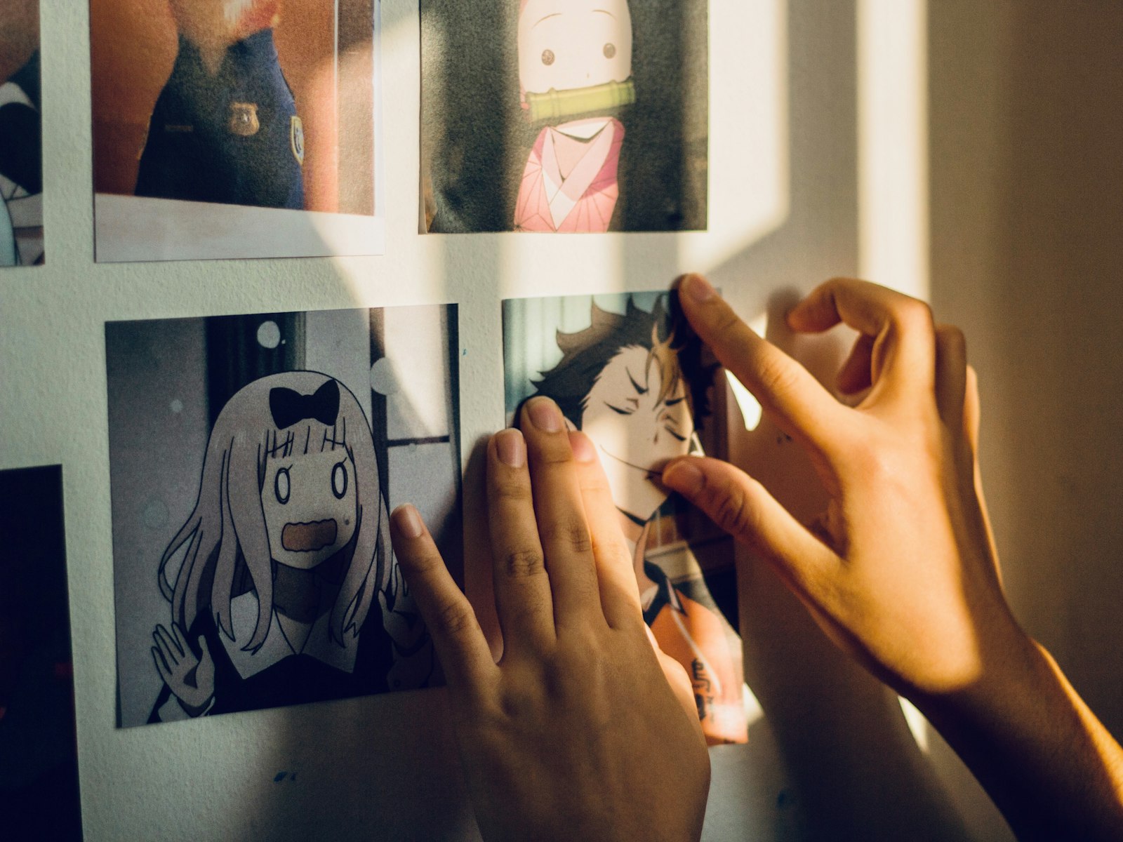 Hands attaching an anime print to a white wall in warm sunlight