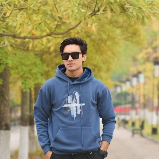 A man in a blue hoodie standing next to a tree